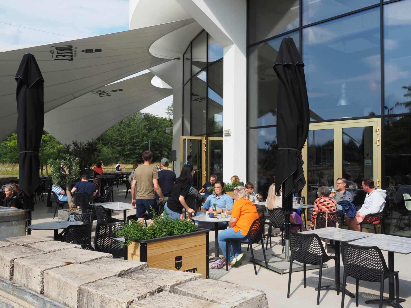 Visitors sit with a drink on the TODI brasserie terrace, under large shade sails.