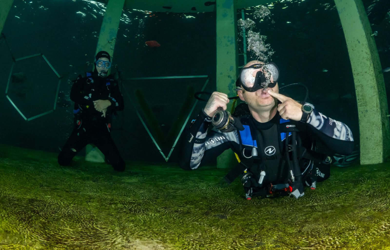 Duikinstructeur demonstreert een oefening onder water bij TODI, terwijl een cursist toekijkt.
